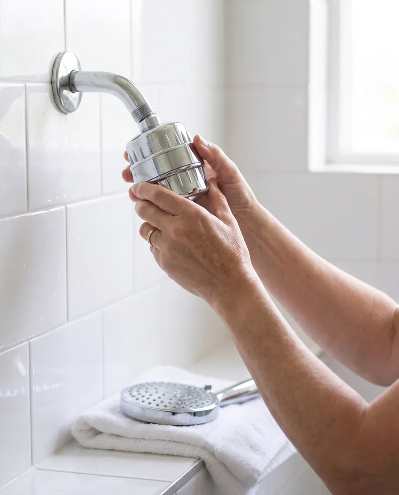 Hands screwing the chrome filter onto a shower arm, the shower head waiting on a folded towel